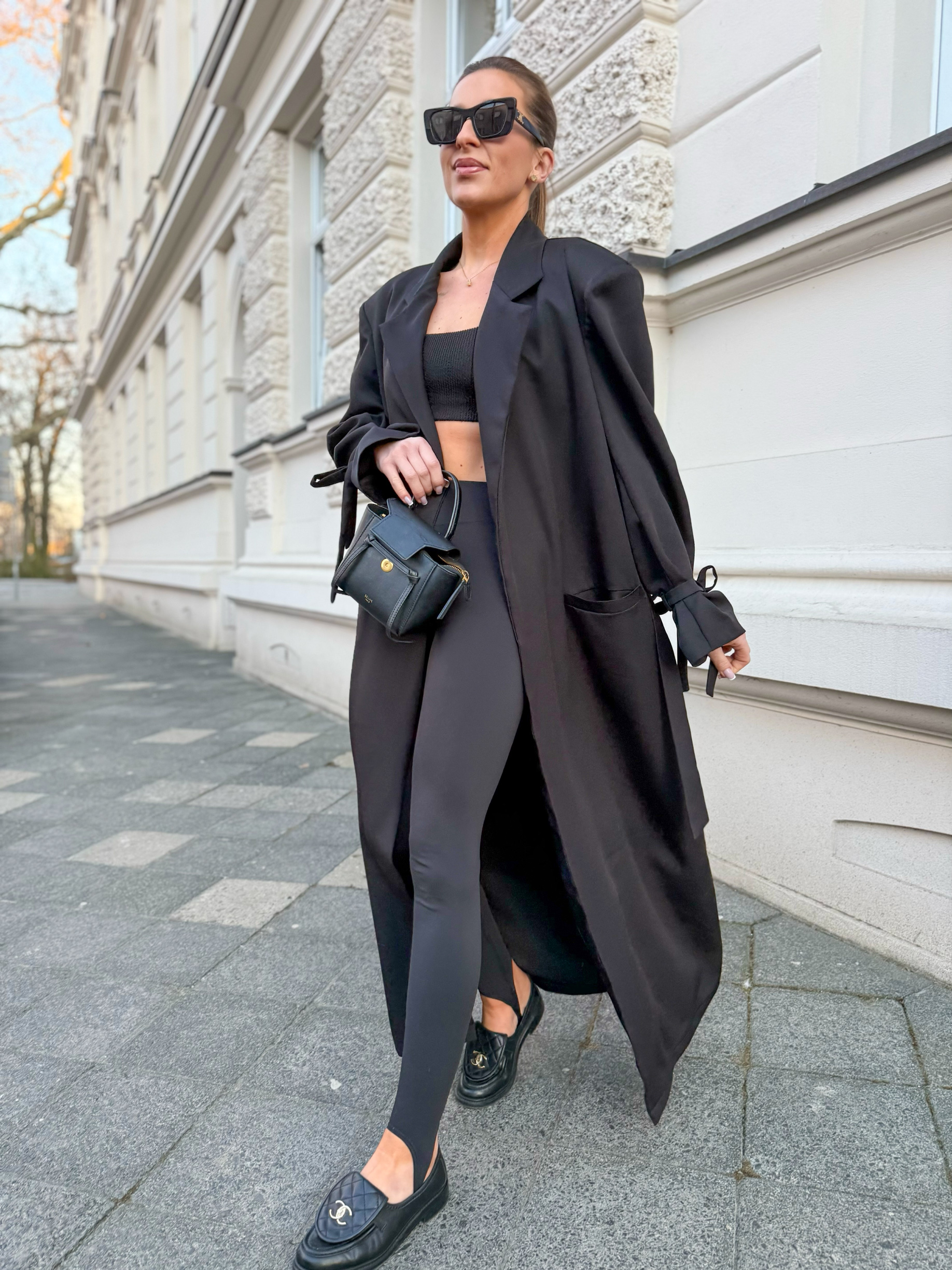 Woman wearing an oversized black blazer with black leggings, a black crop top and quilted loafers