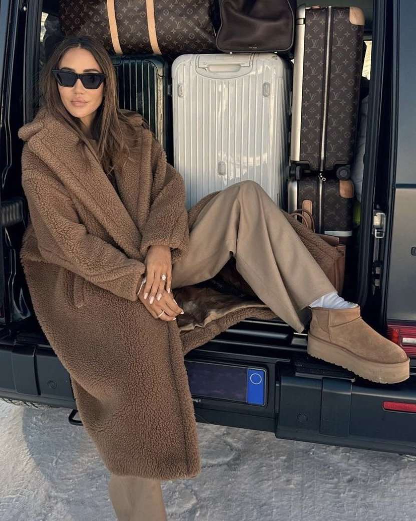 Woman wearing Ugg Tazz platform slippers with charcoal joggers, a hoodie and a camel overcoat