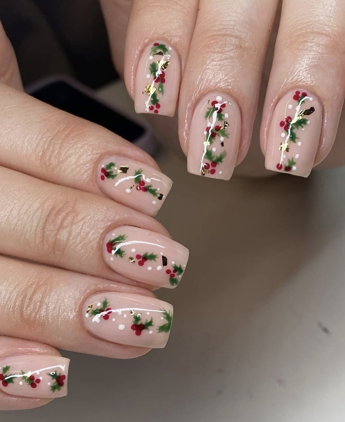 Short square blush-nude nails with holly, red berries and gold foil flecks