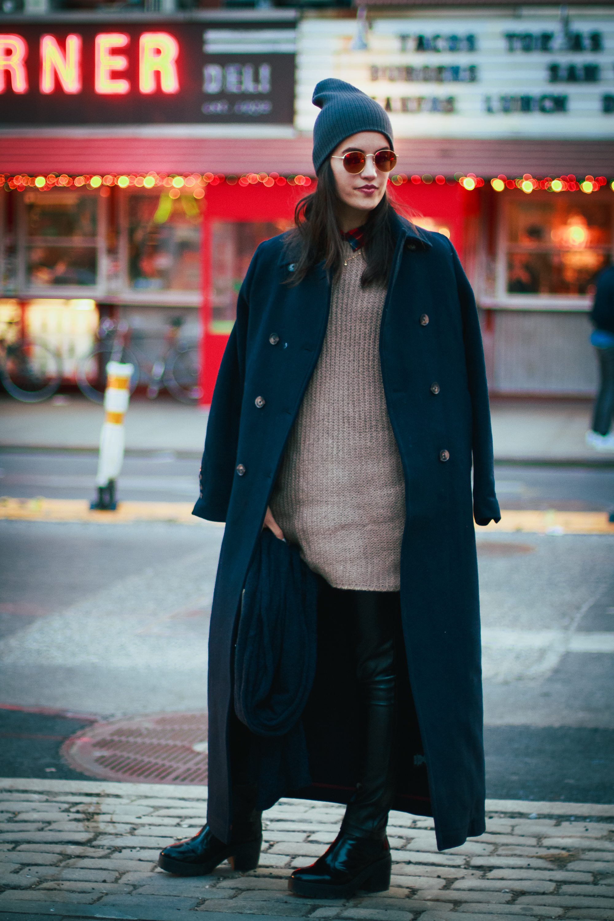 Woman in a grey slouchy beanie, navy coat and over-knee boots at night