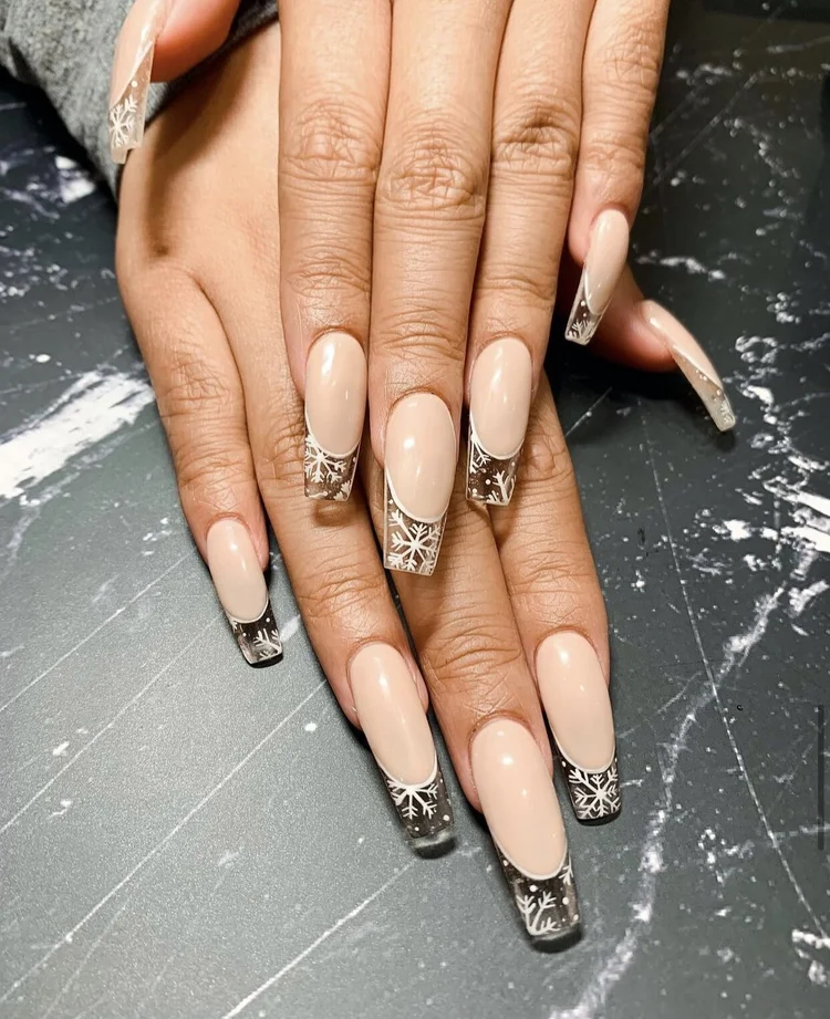 Long coffin nails in sheer nude with clear french tips decorated with white snowflake art