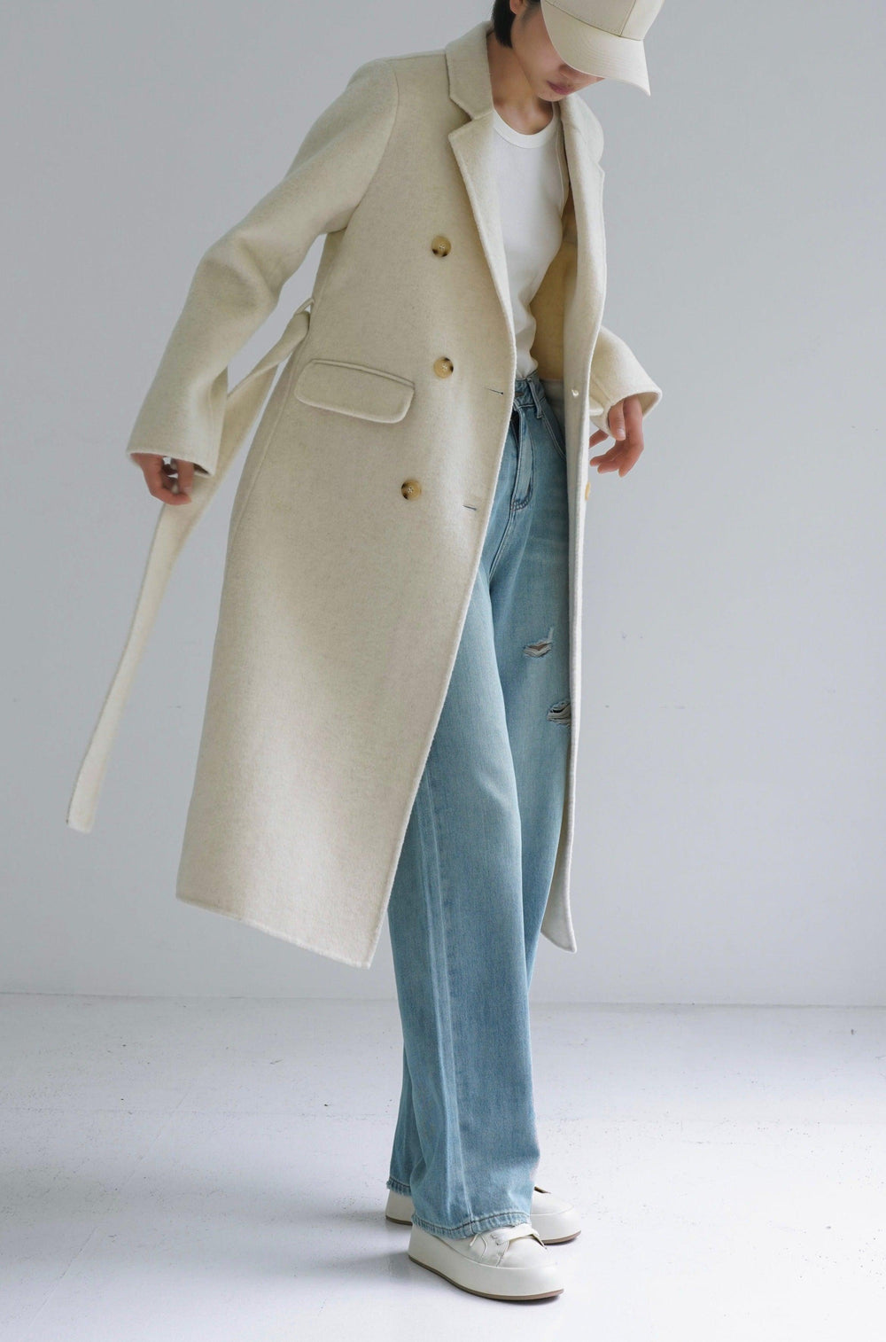 Woman in a cream double-breasted wool coat with white t-shirt, ripped light-wash jeans and white sneakers