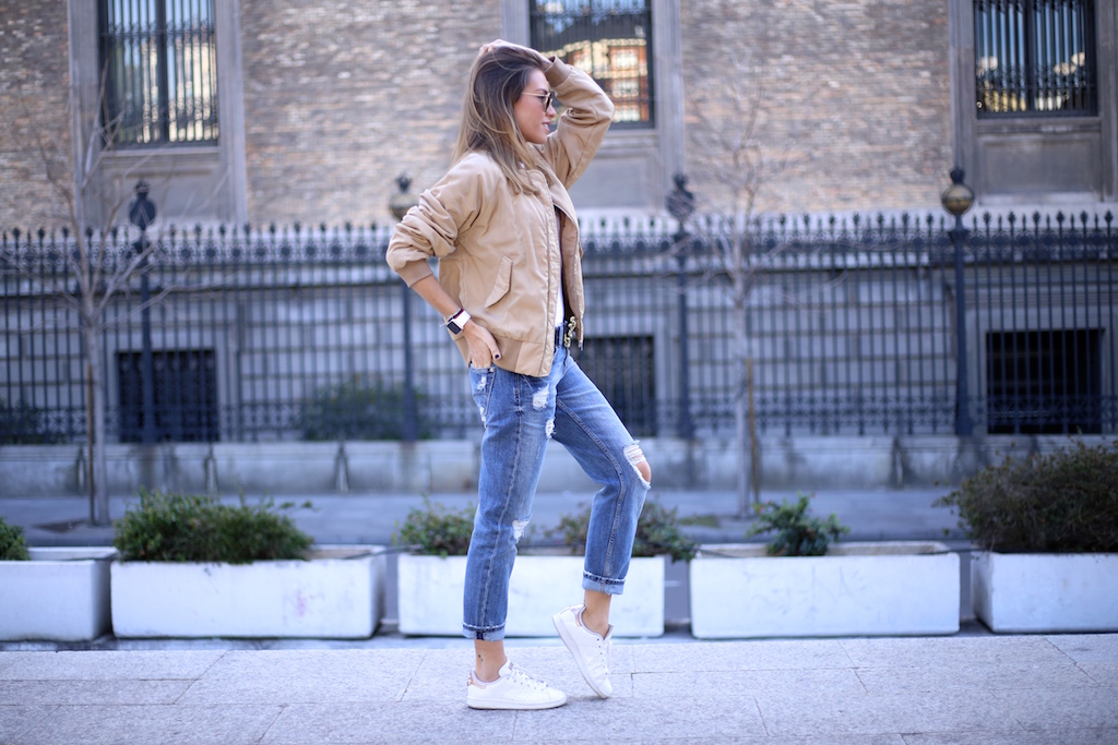 Woman in a tan utility jacket, white top, ripped boyfriend jeans and white sneakers