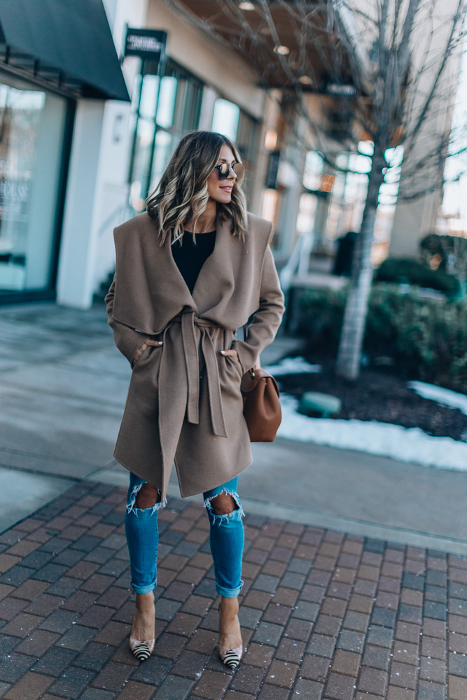 Woman wearing a camel wrap coat with ripped blue jeans and striped flats