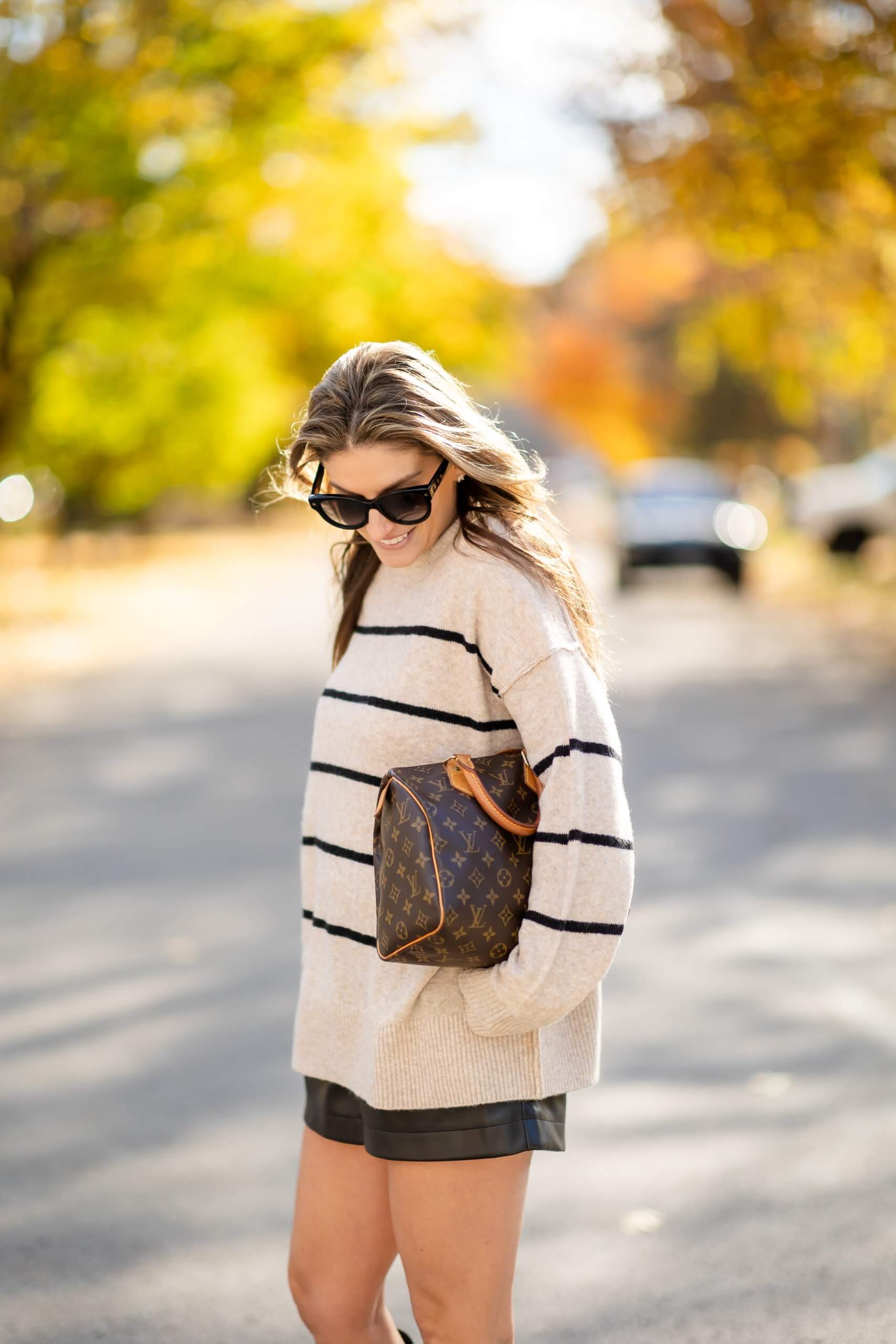 Woman wearing an oatmeal striped mock-neck sweater with black leather shorts and a monogrammed handbag