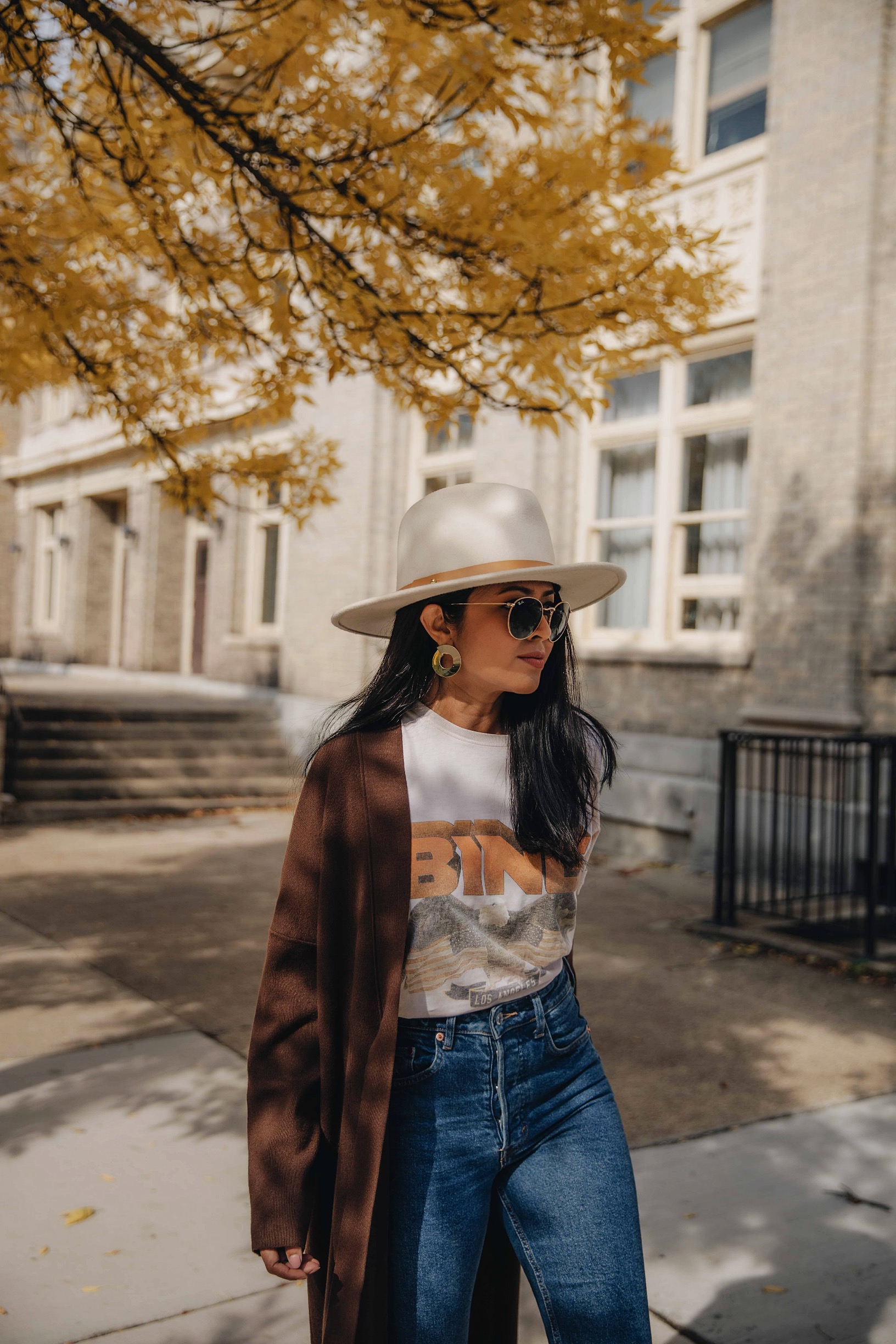Woman in a long brown cardigan with a white graphic tee, mom jeans, and a felt hat