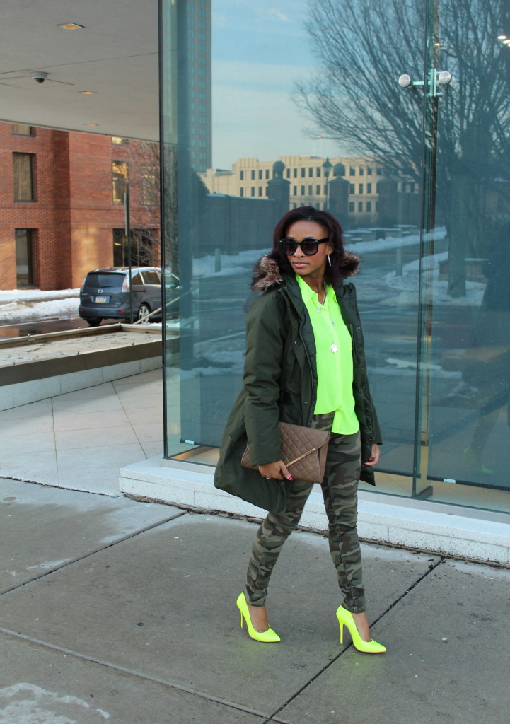 Woman in a green parka with a neon yellow top, camo leggings and neon heels