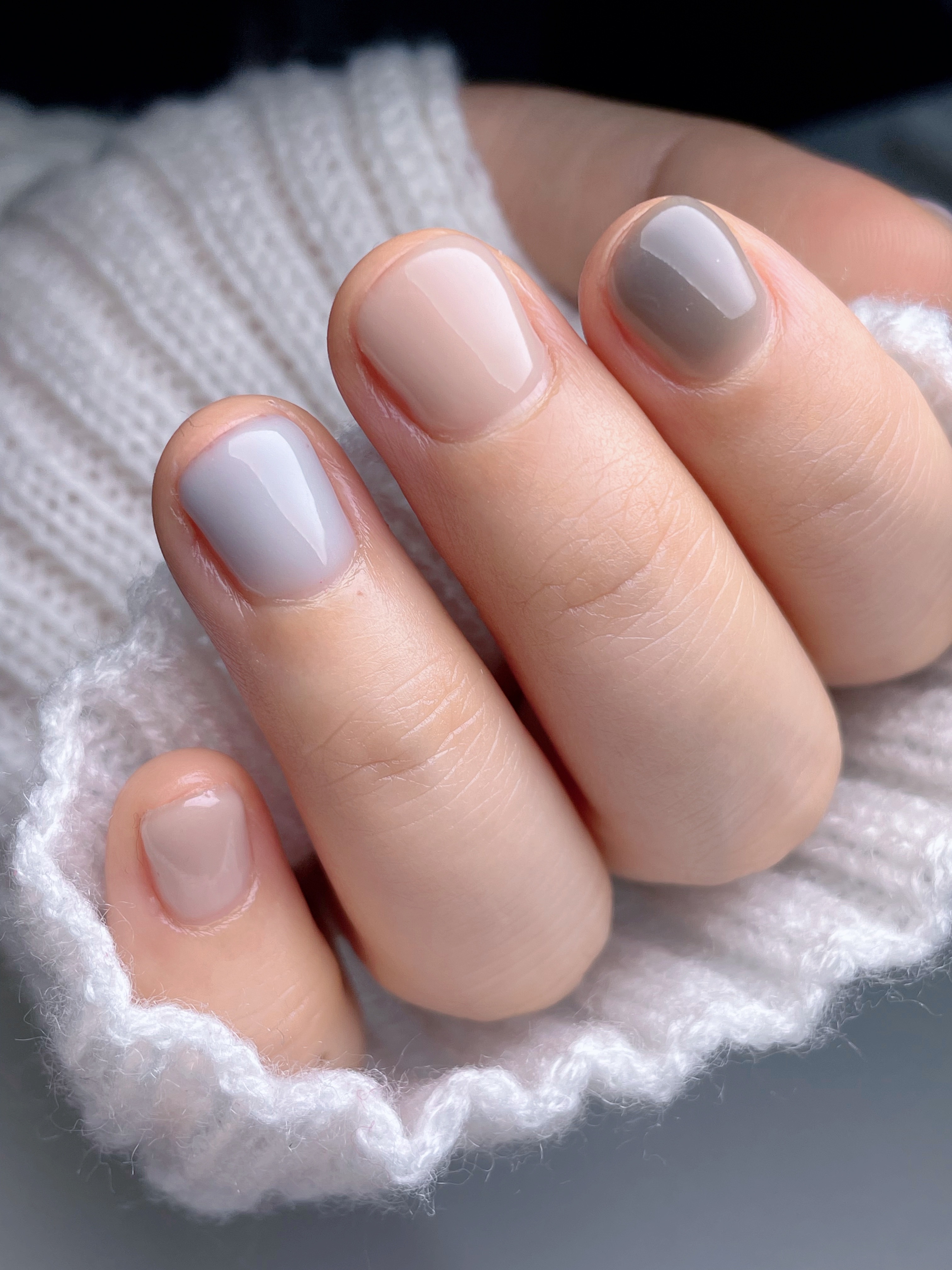 Short round nails in a mix of sheer nude, light gray and taupe shades