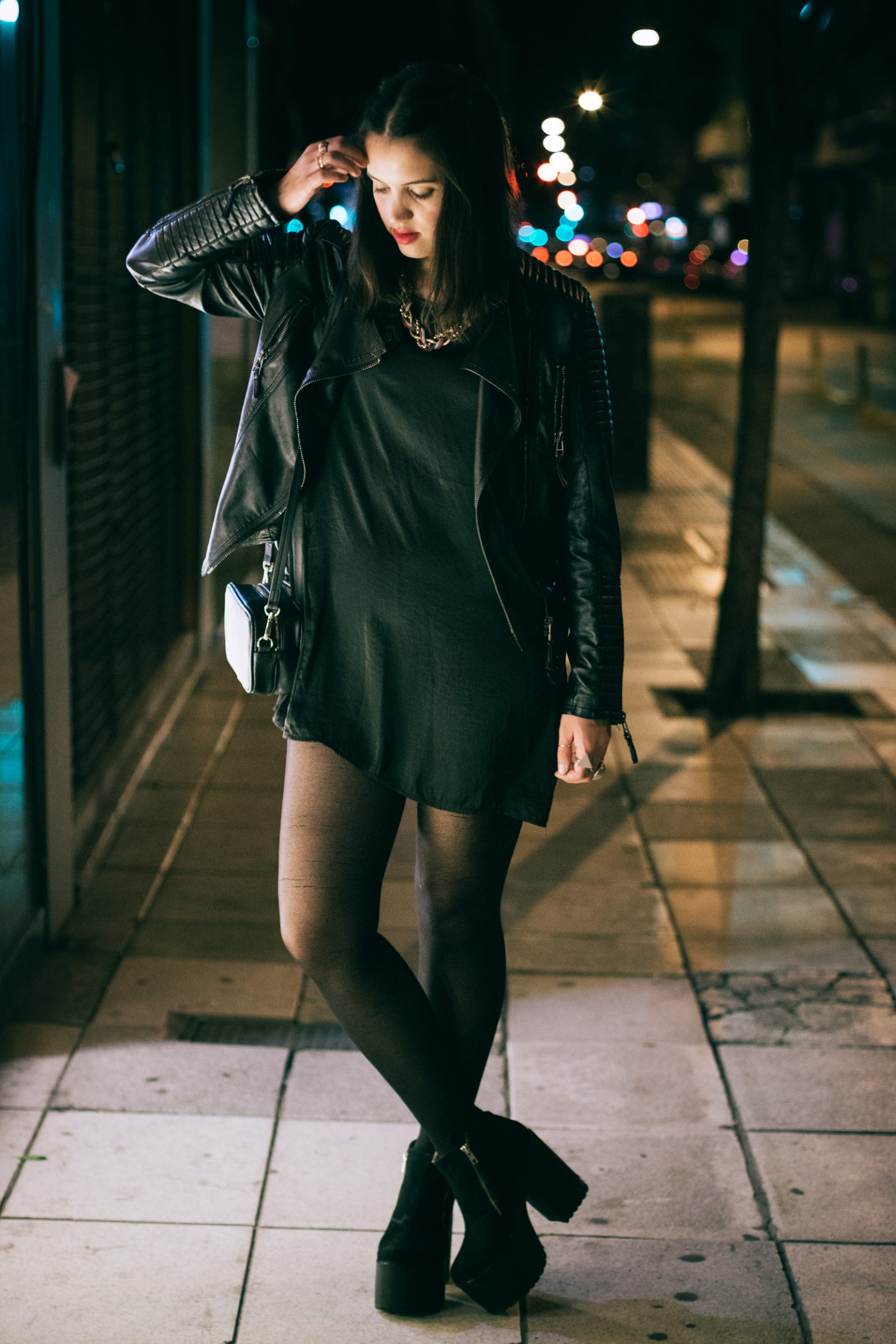 Woman at night in a black dress, black leather jacket and black platform block-heel boots