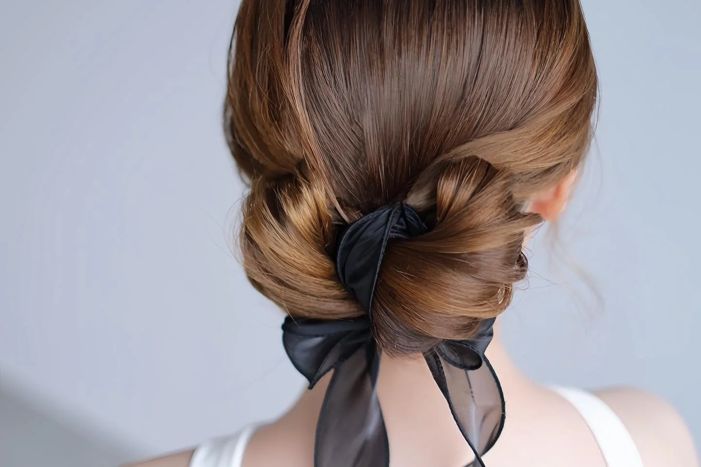 Back view of a low knot bun tied with a black satin ribbon