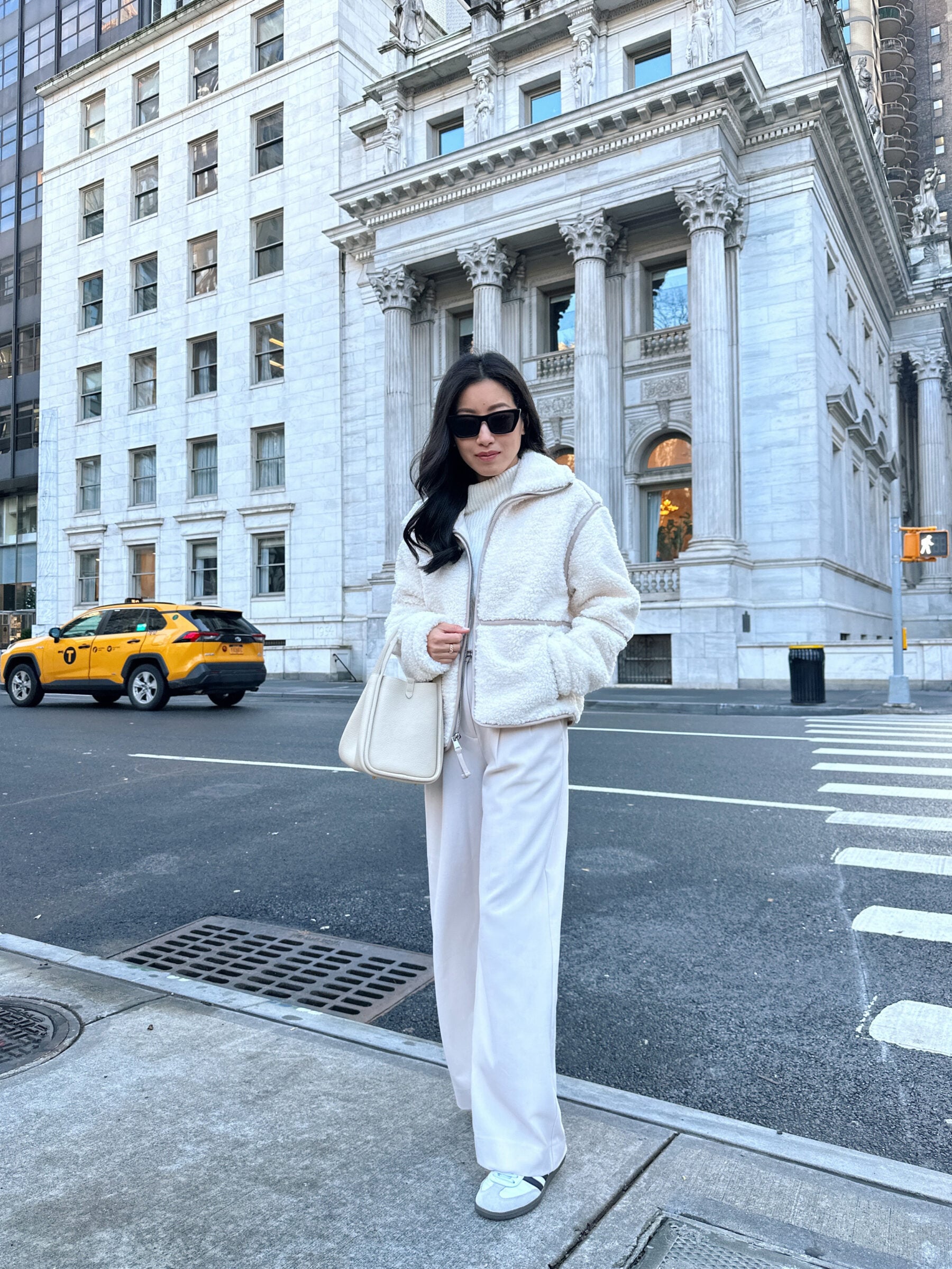 Woman in a white sherpa jacket and white wide-leg trousers with sneakers on a city street