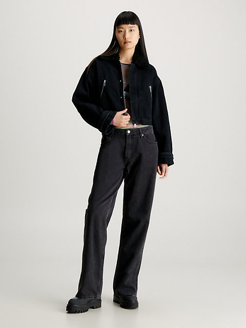 Woman wearing a black denim jacket with a dark shearling collar, graphic tee, black wide-leg jeans and chunky boots