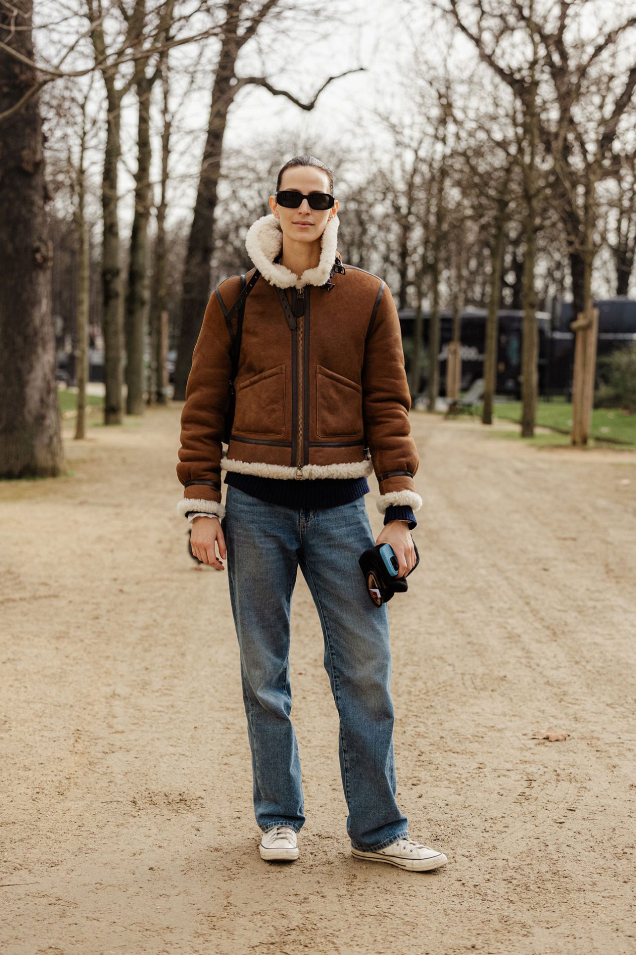 Woman in a brown shearling aviator jacket, straight-leg blue jeans and white canvas sneakers