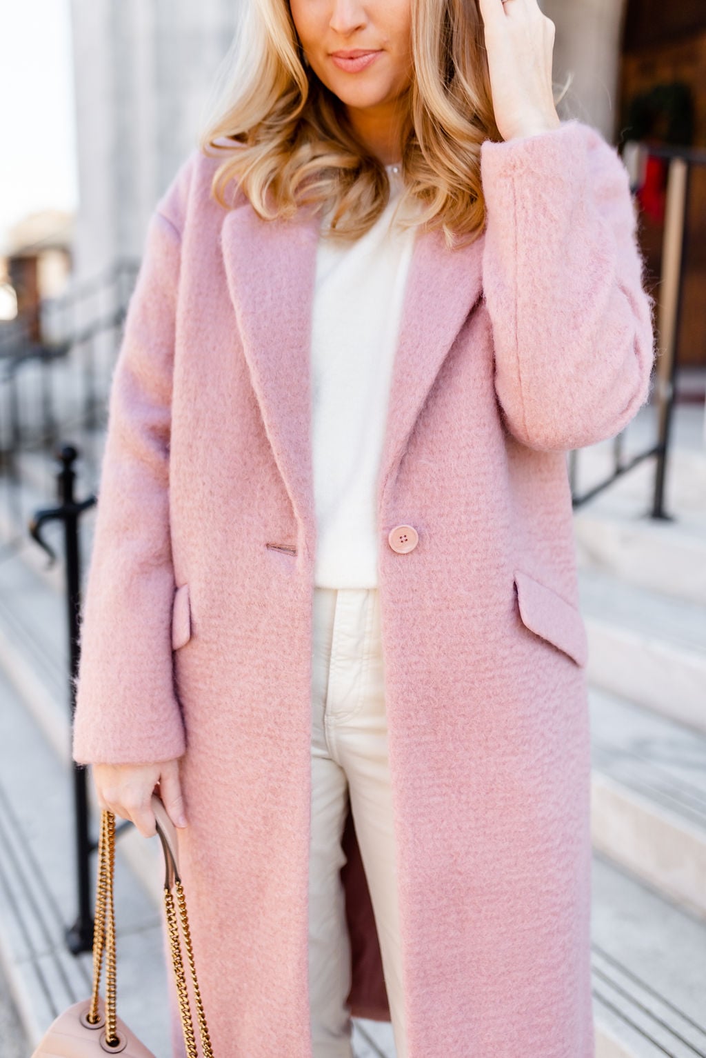 Woman wearing a pastel pink coat over a cream and white winter outfit