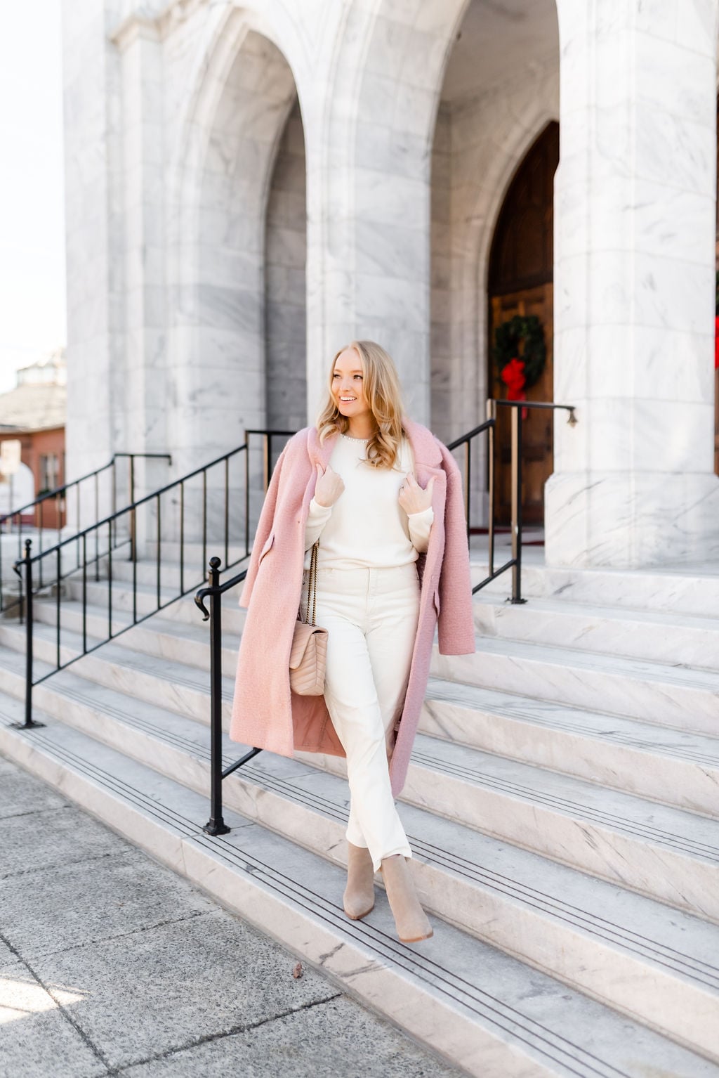 Woman wearing a blush pink textured wool coat over a white sweater and white jeans with beige ankle boots
