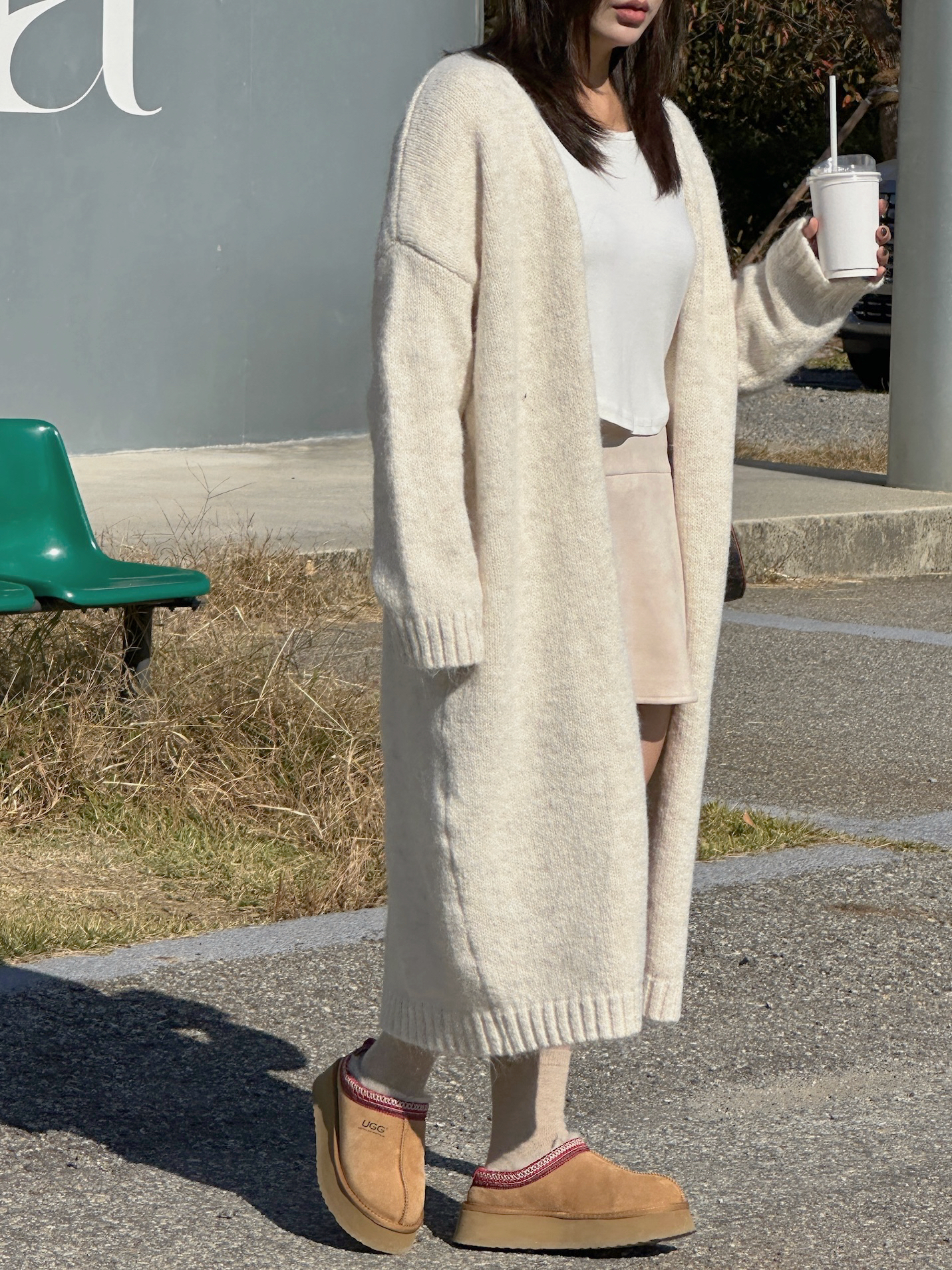 Woman wearing chestnut Ugg Tazz platform slippers with a longline cream cardigan, white tee and suede mini skirt
