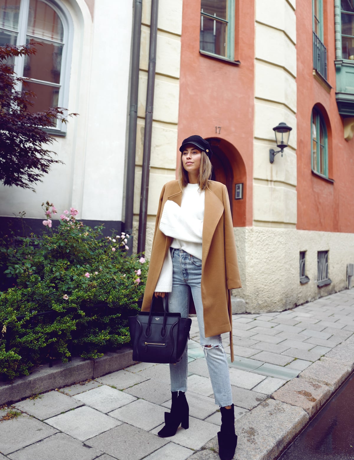 Woman in a camel coat, white knit sweater, light-wash jeans and black ankle boots on a city street