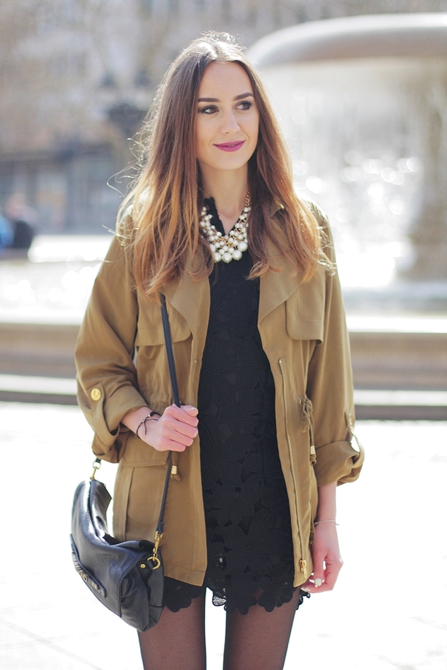 Woman in a short tan parka over a black lace dress with a pearl necklace
