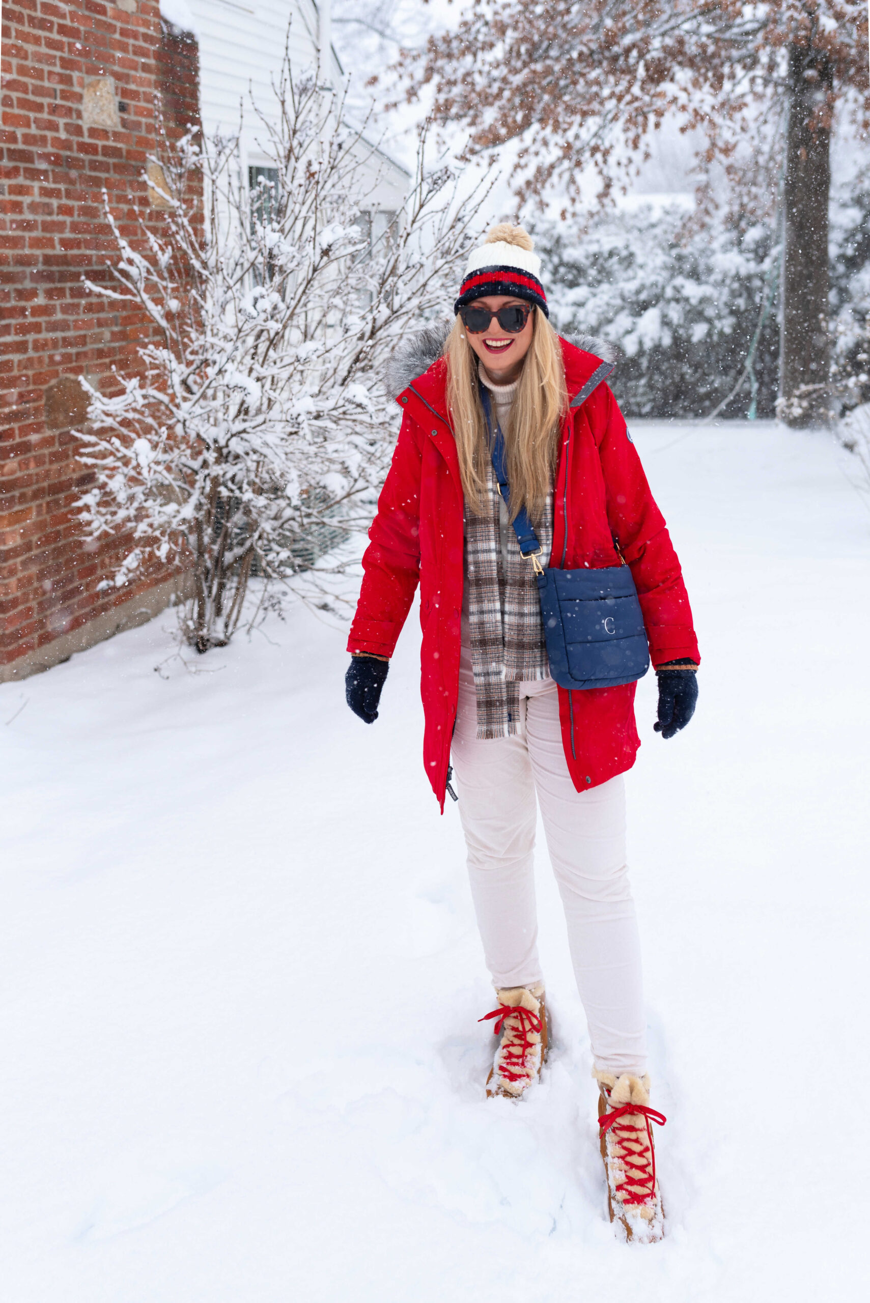 Woman in a red parka with a plaid scarf, white jeans and snow boots in the snow