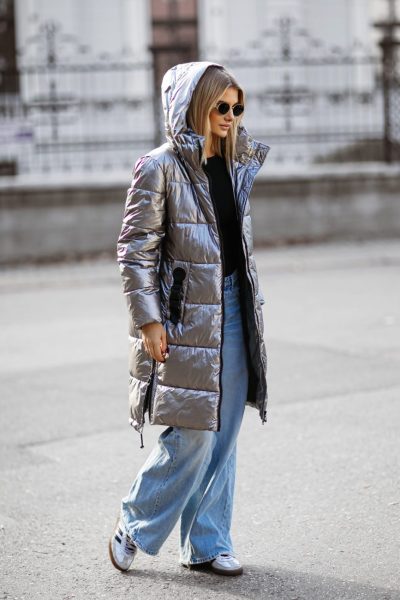 Woman wearing a long silver metallic puffer coat with wide-leg jeans and sneakers