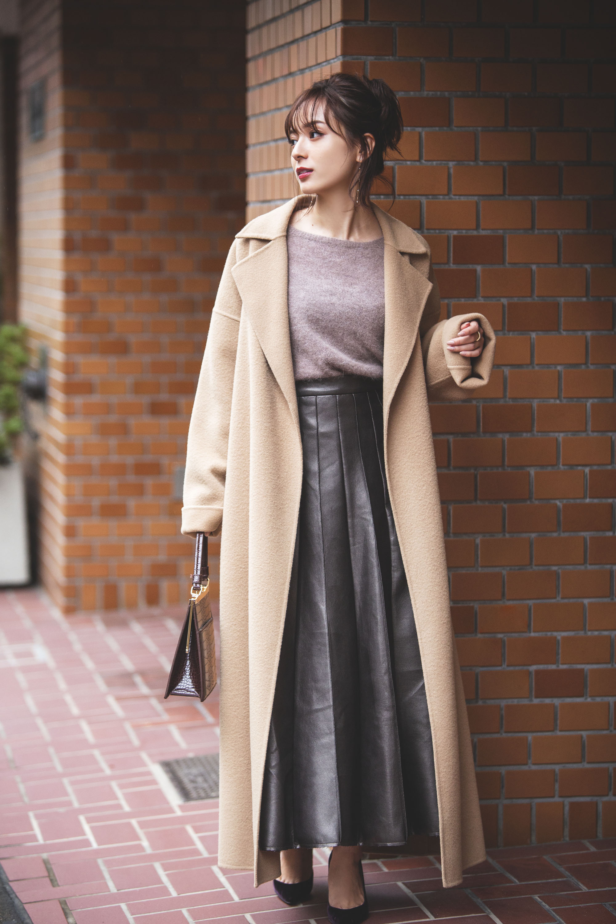 Woman in camel coat with mauve knit and black leather pleated midi skirt
