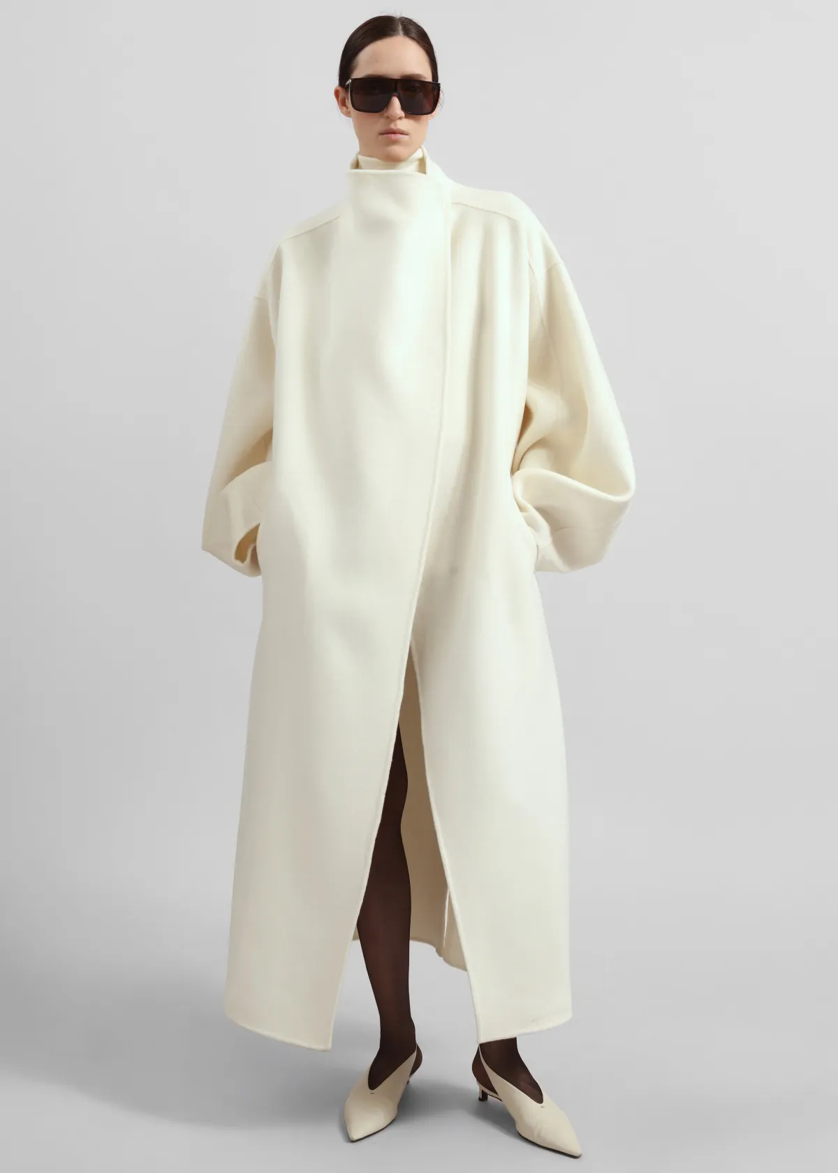 An oversized cream wrap coat worn with a cream turtleneck, sheer tights, cream slingback heels and oversized sunglasses.