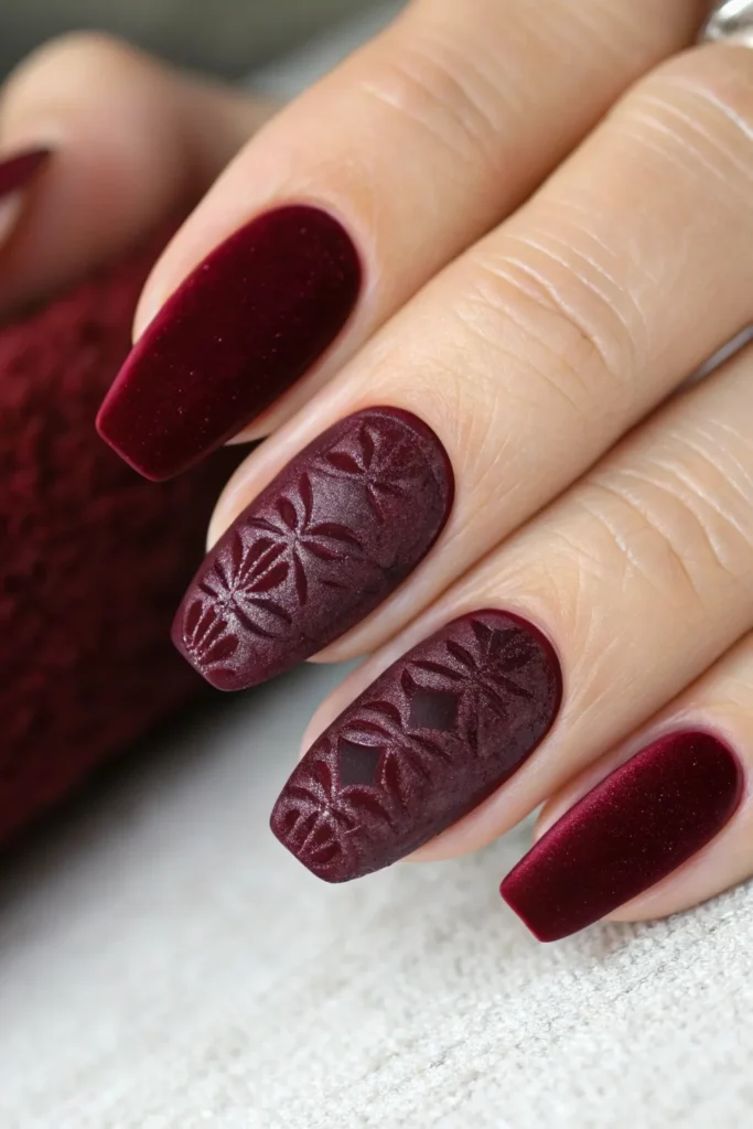 Matte velvet burgundy nails with embossed floral texture on two accent nails