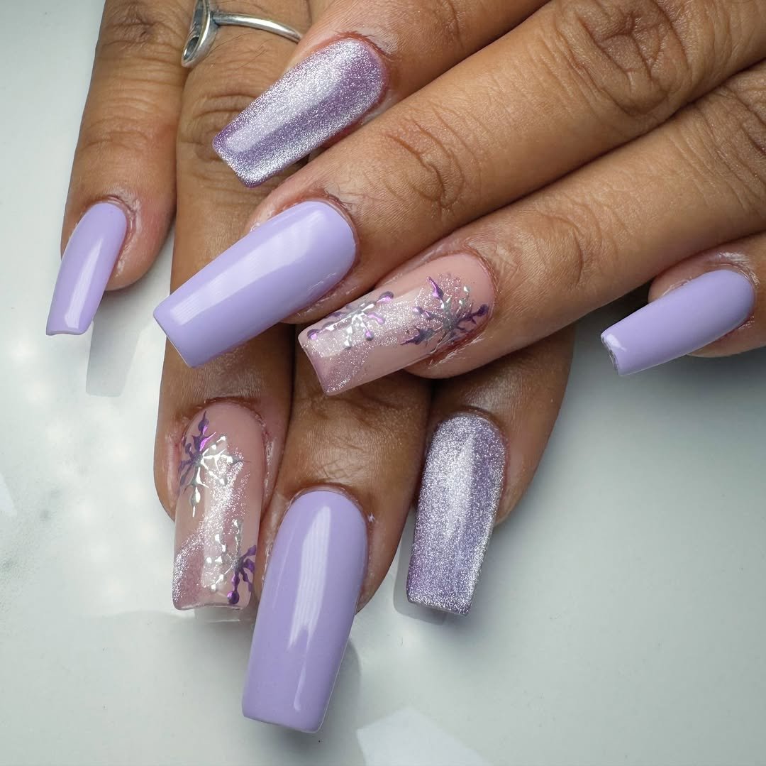 Long square nails in lavender with cat-eye shimmer, silver glitter and purple snowflake art on accent nails; real photography.