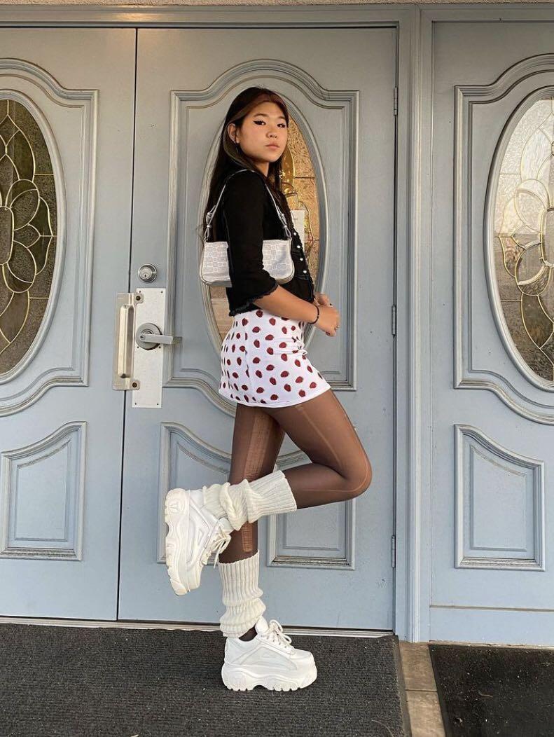 White scrunchy leg warmers with a white cherry print mini skirt, black top and chunky white sneakers