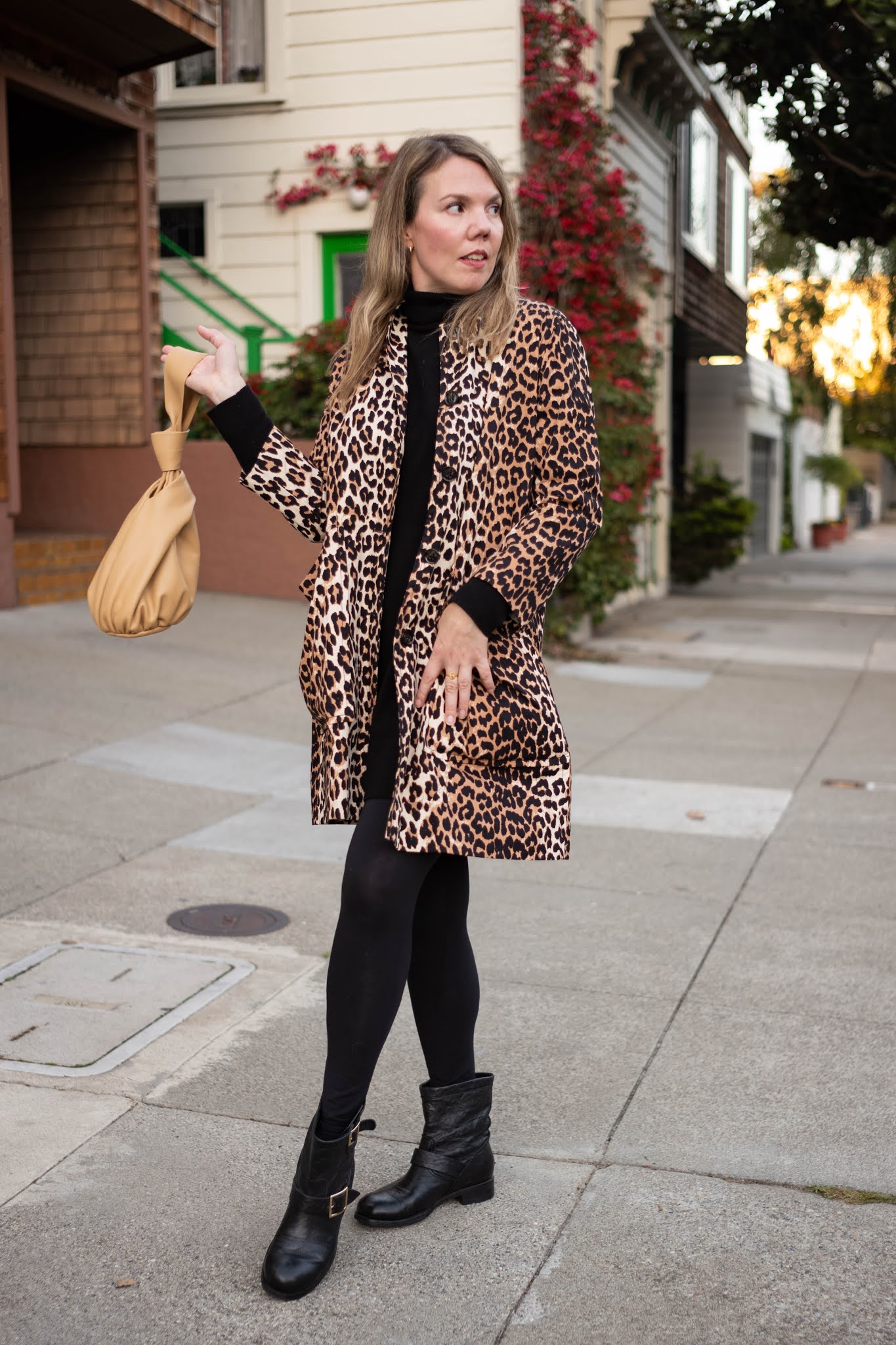Woman in a leopard print coat, black turtleneck, black tights and black buckled ankle boots