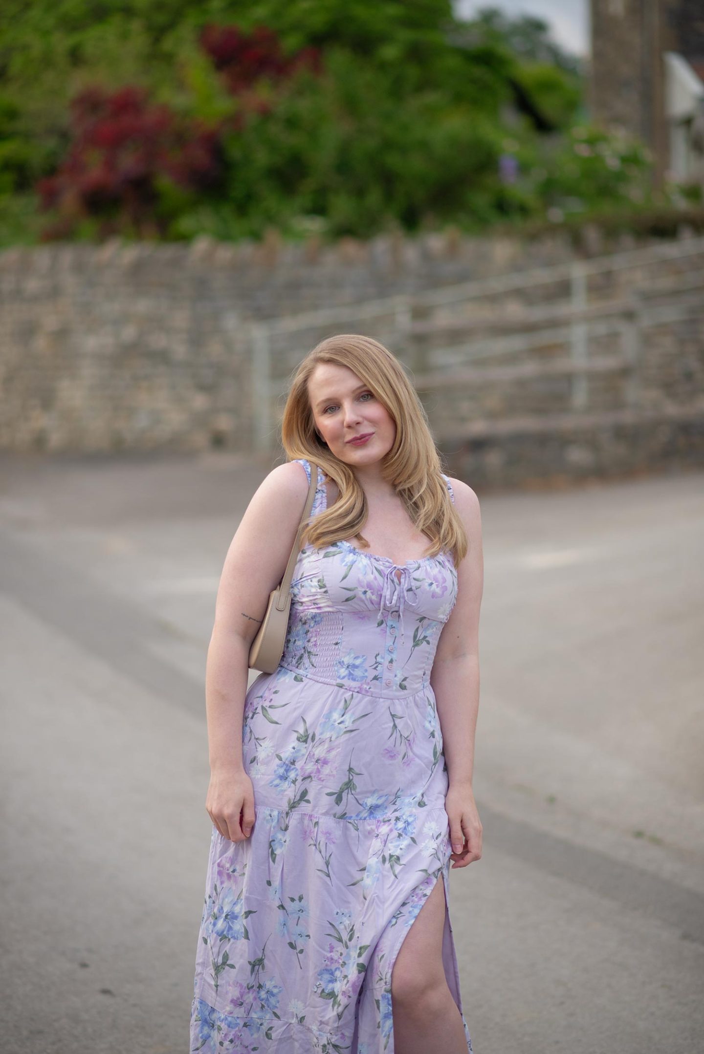 Woman wearing a lilac floral midi dress with beige shoulder bag outdoors