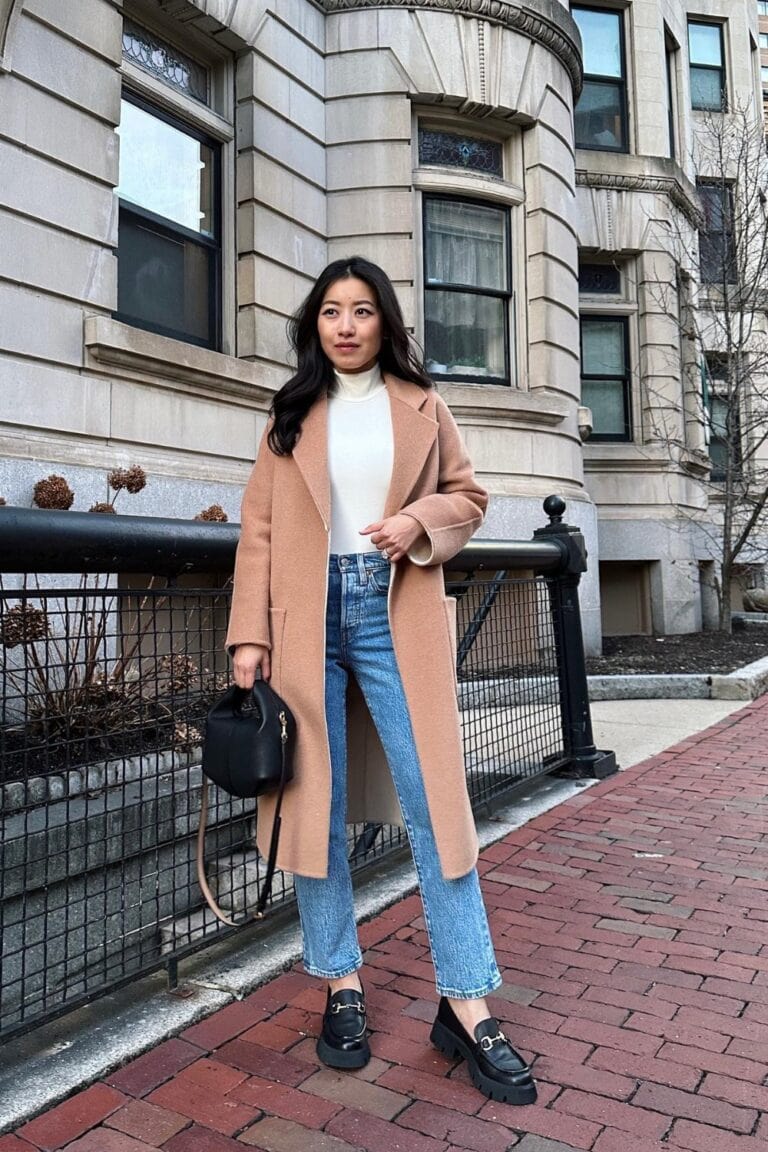 Woman in a camel coat with white sweater and jeans
