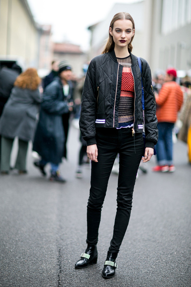 Woman in a black quilted bomber jacket, striped knit, black skinny jeans and embellished black ankle boots