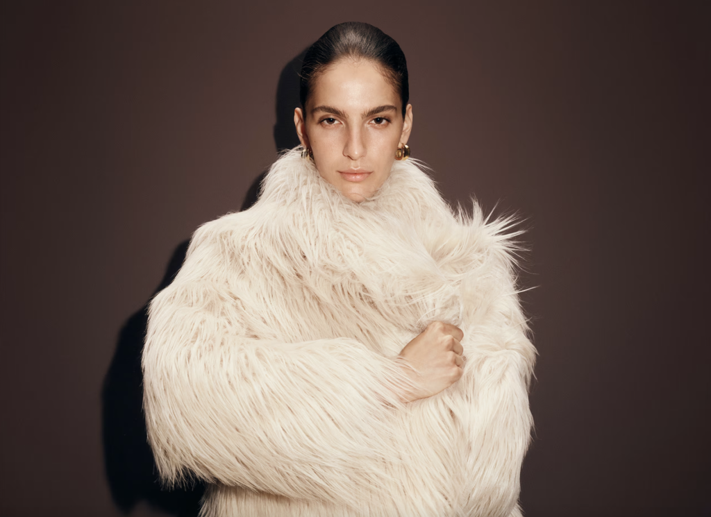 Woman wearing a voluminous white faux-fur coat in a studio portrait