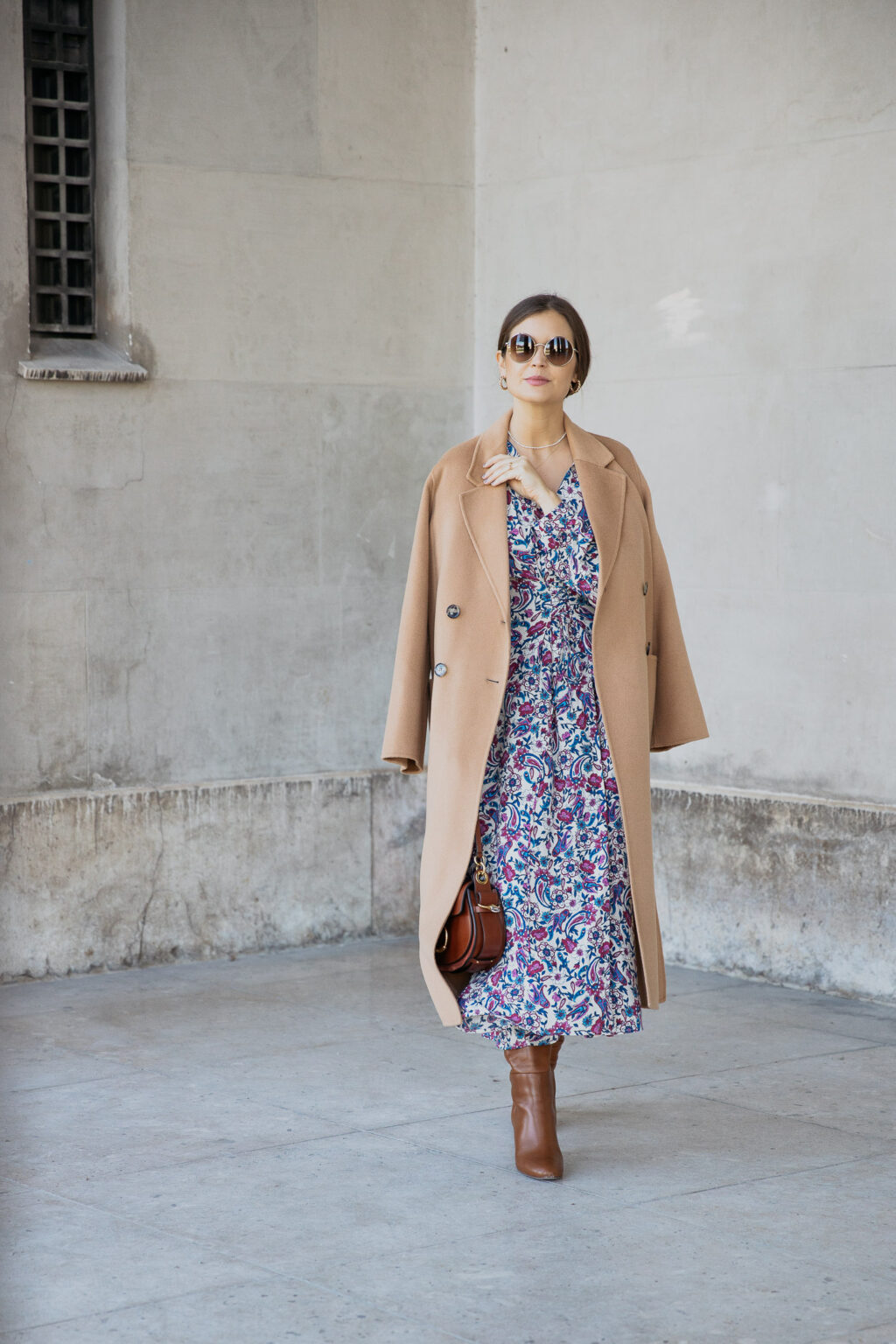 Woman wearing a camel coat over a blue and pink floral midi dress with brown knee-high boots