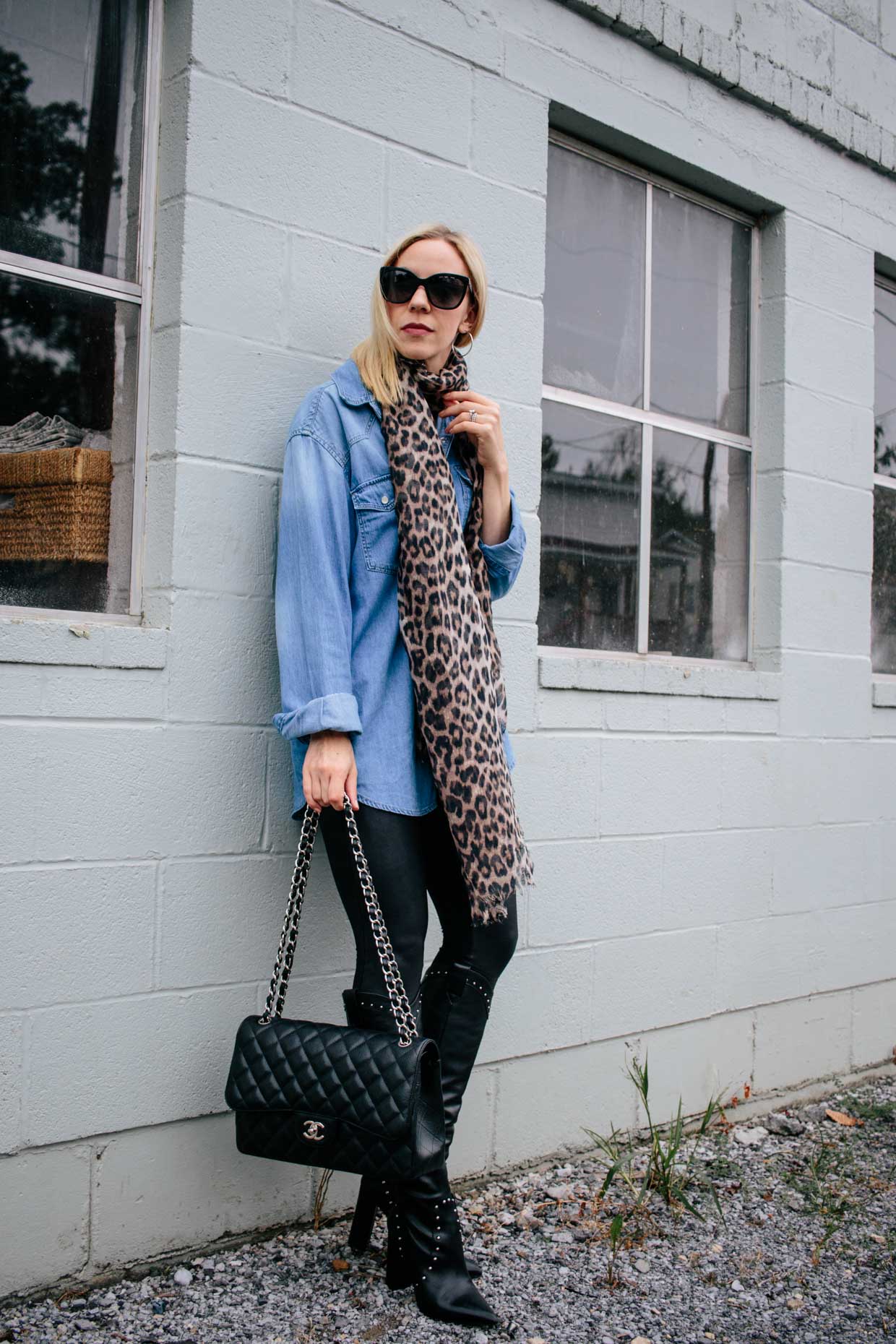 Woman in a leopard scarf, oversized light-blue denim shirt, black leather leggings and studded knee-high boots