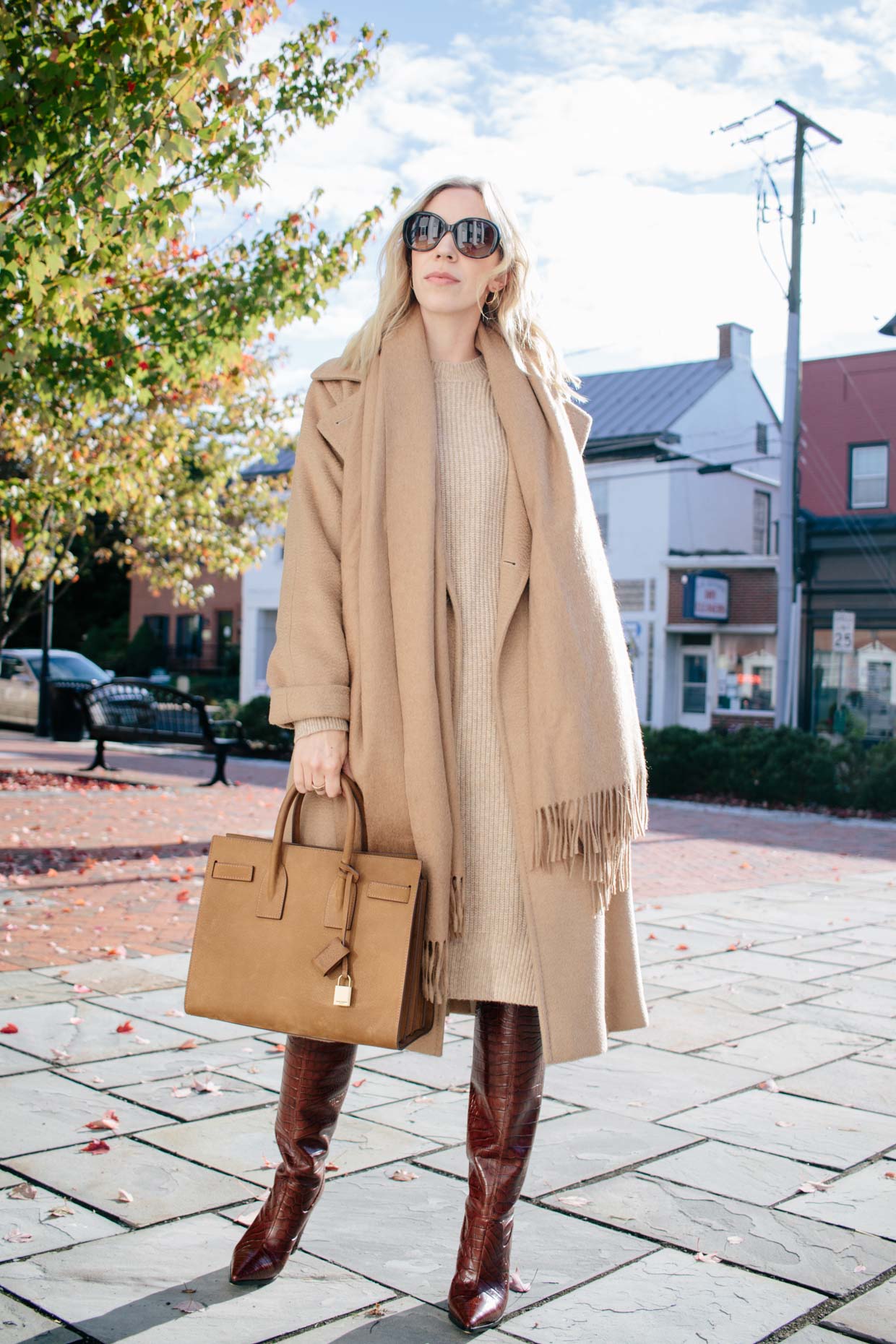 Woman in a belted Max Mara camel coat over a camel knit midi dress with brown croc knee-high boots
