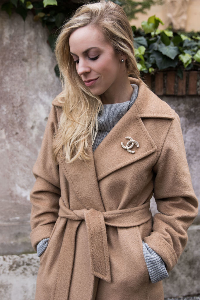 Belted camel wrap coat with a gray knit and a sparkling brooch at the lapel