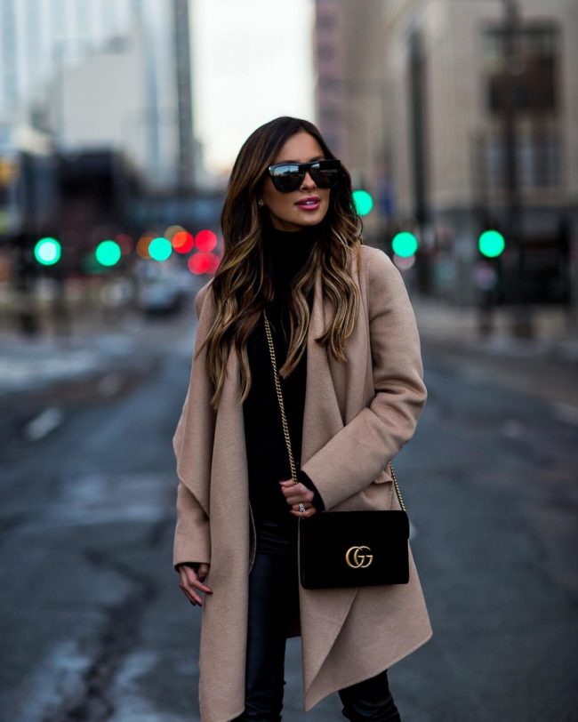 Woman wearing a camel wool coat over a black turtleneck with black pants on a city street