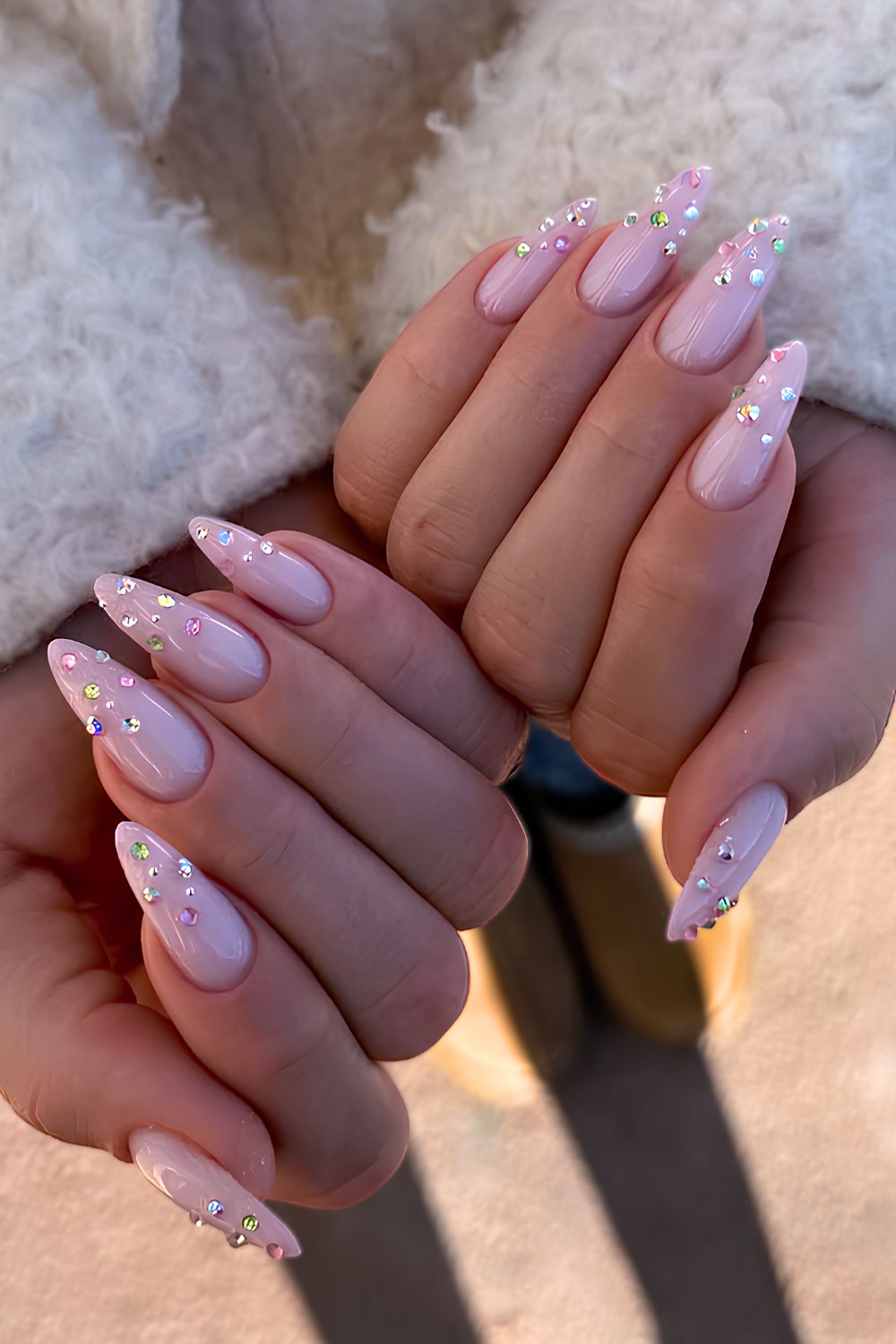Long stiletto nails in milky pink with multicolor rhinestones scattered toward the tips