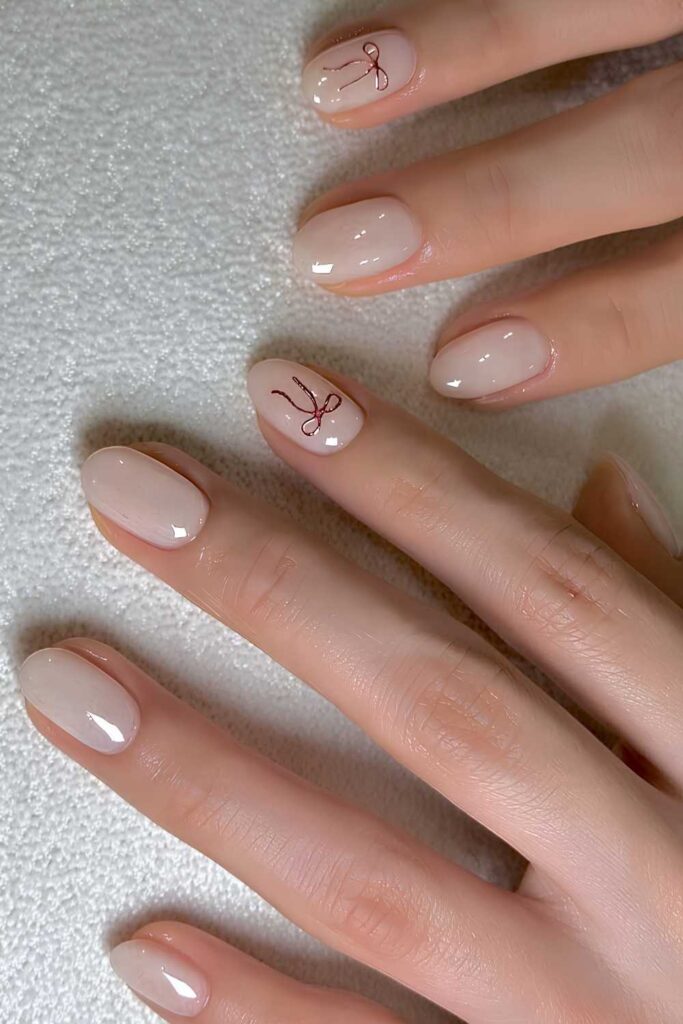 Short oval milky white nails with tiny red hand-painted bows on two accent nails