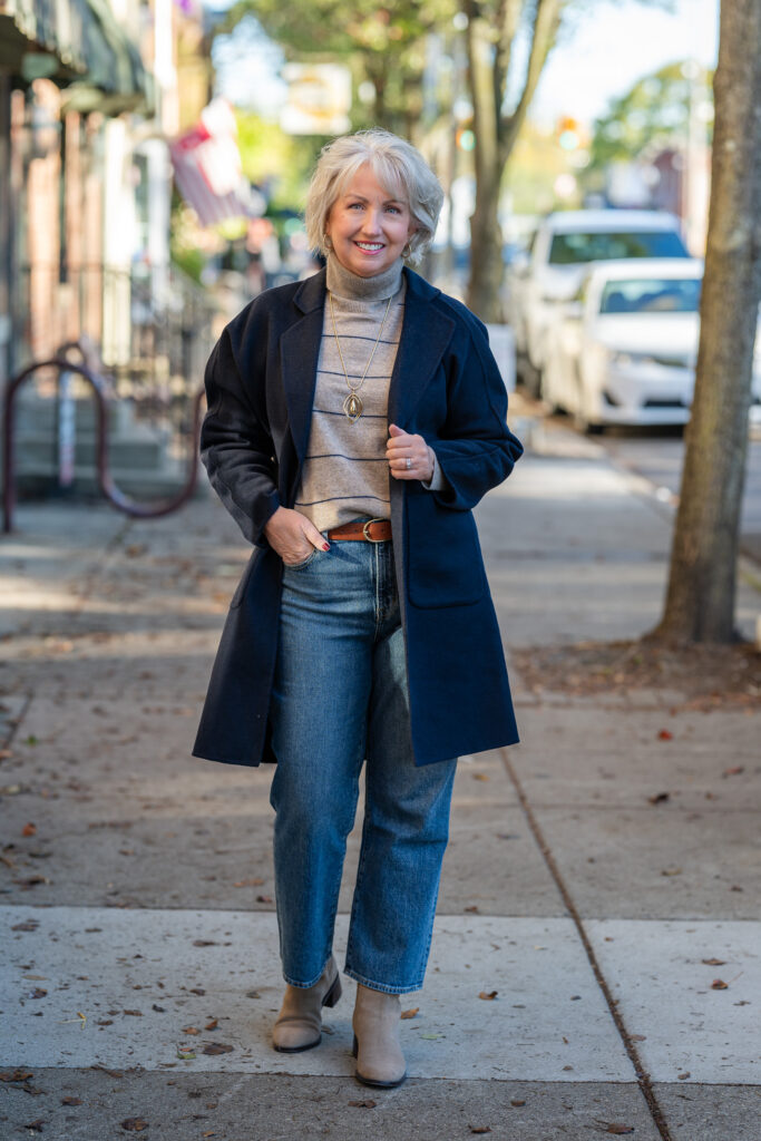 Older woman in a navy peacoat over a striped Breton top with dark jeans