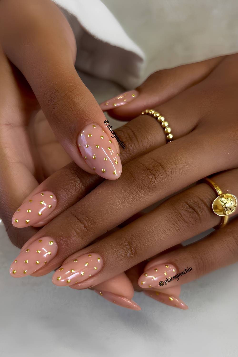 Almond nails in a nude peach base covered with small gold chrome polka dots