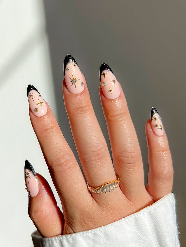 Nude almond nails with black french tips and gold starburst art