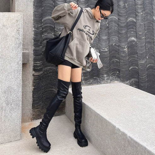Woman in oversized taupe hoodie, black shorts and over-the-knee boots