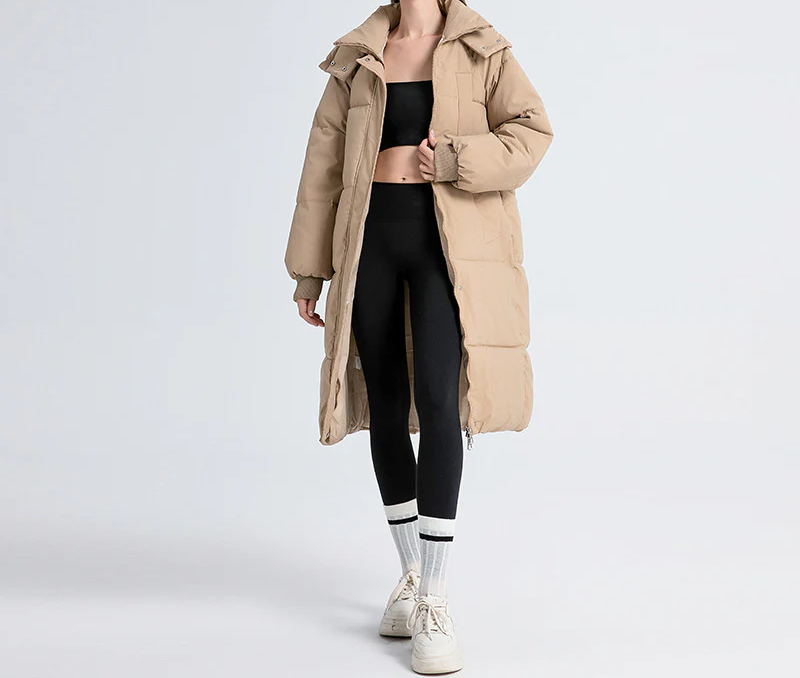 A woman wearing a long puffer coat with a hoodie and sneakers