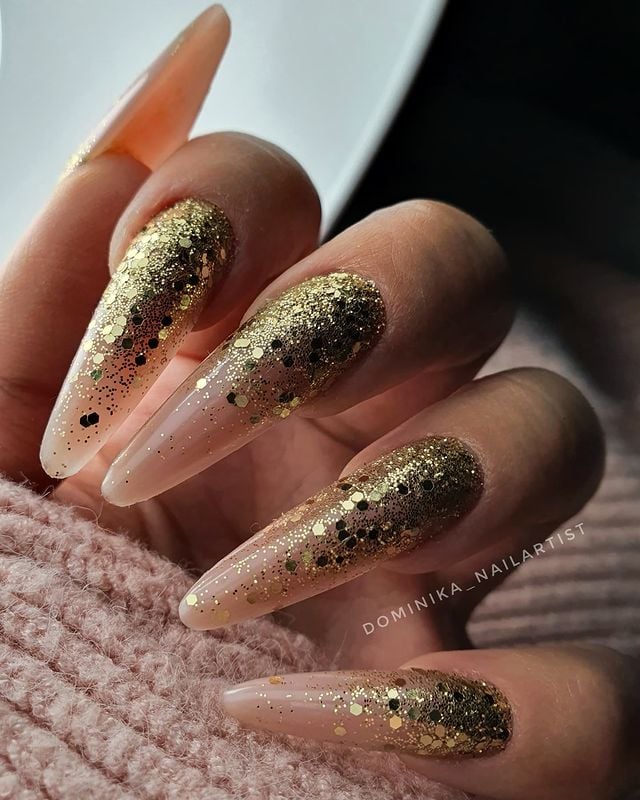 Almond-shaped nails with a nude base fading into gold glitter toward the tips