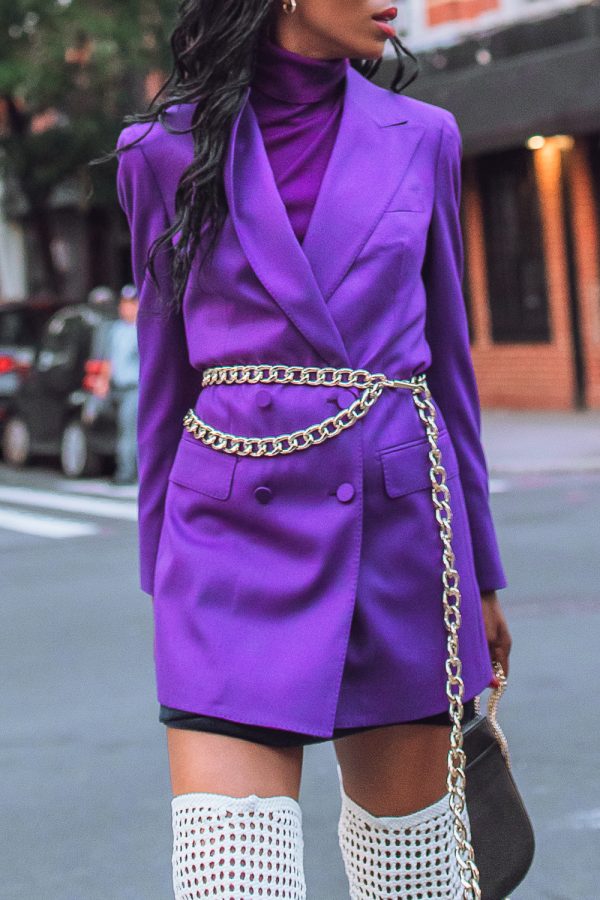 Woman in a vivid purple blazer over purple turtleneck with gold chain belt and black skirt
