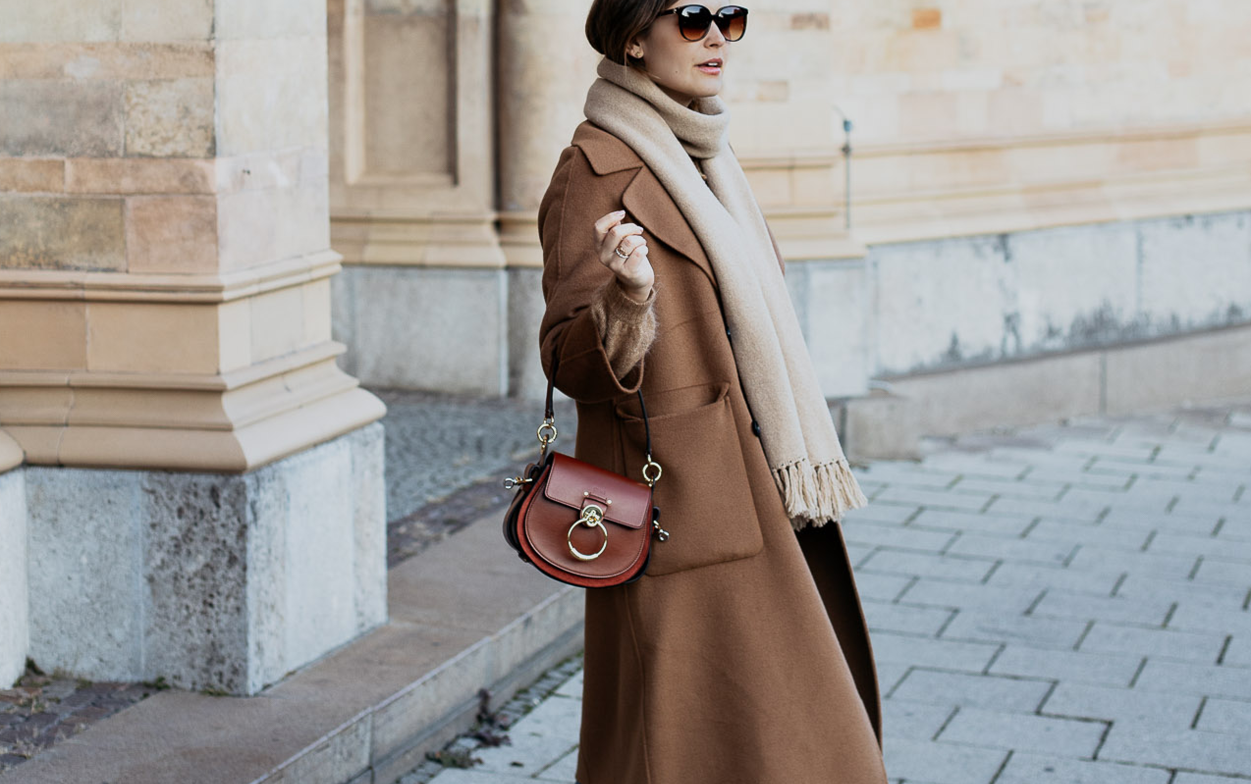 Woman wearing a camel coat with a cardigan and jeans in a winter street look