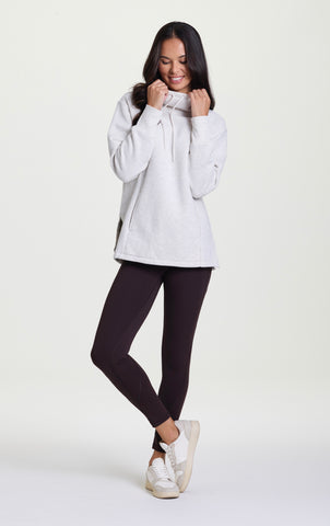 Woman in light gray oversized hoodie, dark brown leggings and white sneakers